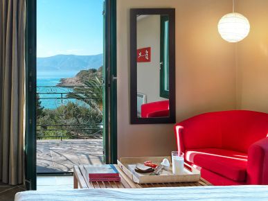 A serene bedroom with an open door leading to a balcony, where the ocean view complements a cozy breakfast setup by the sea.